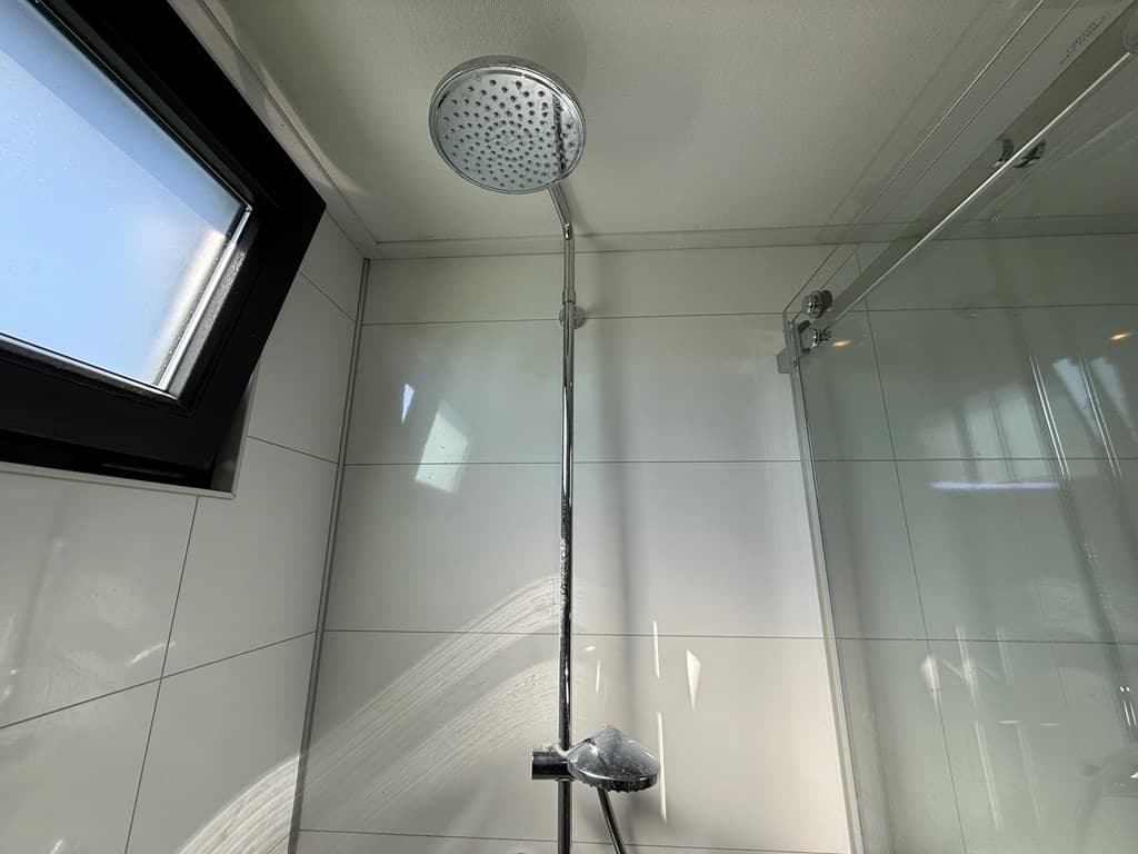 Douche met een regenkop in een moderne badkamer met betegelde wanden en een glazen douchewand.