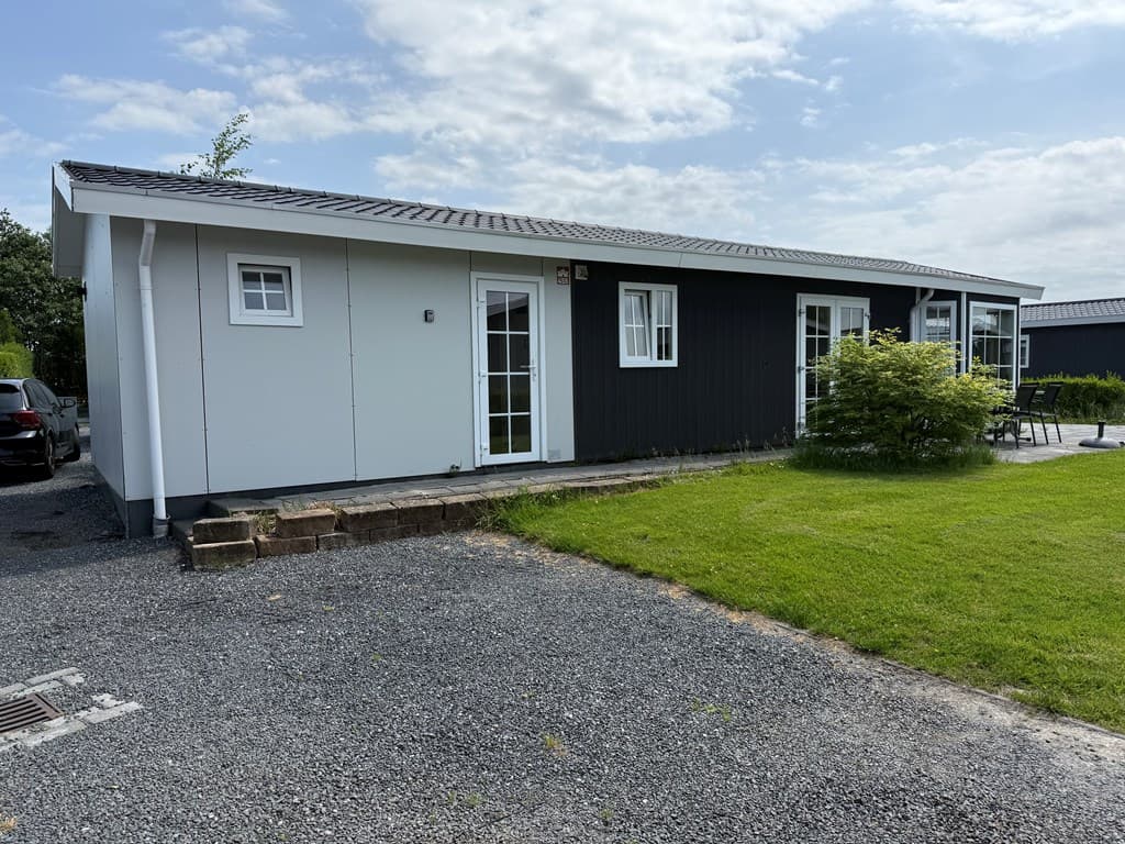 Vakantiewoning met een zwarte en witte gevel, stenen paden en groene graspartij, omringd door een rustige omgeving