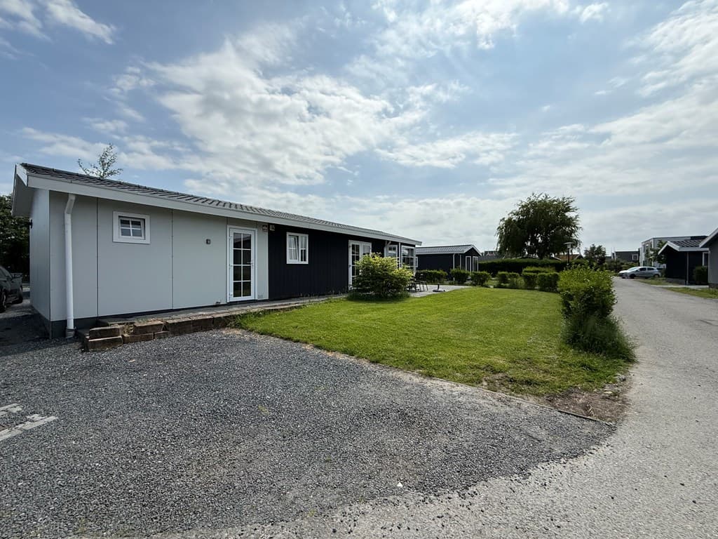 Buitenaanzicht van een vakantiewoning met tuin, grijze oprit en groene planten rondom op vakantiepark De Beemster.