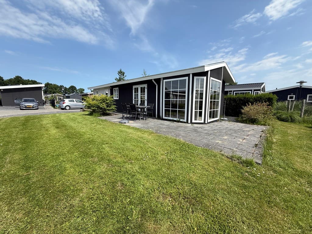 Zwarte vakantiewoning met glazen schuifdeur, gelegen op een grasveld omringd door groen, bij Vakantiepark De Beemster.