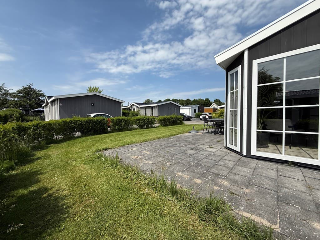 Uitzicht op een betegeld terras met tuinmeubilair en de groene omgeving rondom de vakantiewoningen in een vakantiepark.