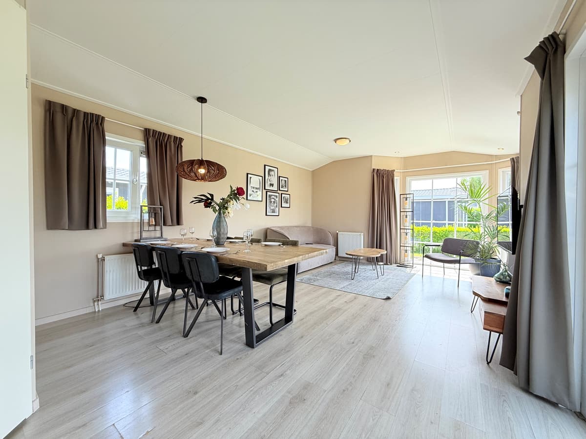 Hedendaagse woonkamer met eettafel, stoelen, bank en planten in een vakantiewoning met grote ramen en neutrale kleuren