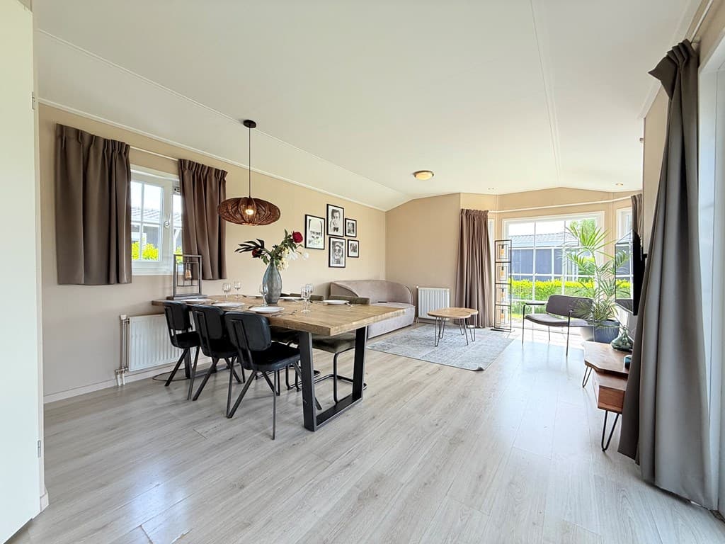 Hedendaagse woonkamer met eettafel, stoelen, bank en planten in een vakantiewoning met grote ramen en neutrale kleuren