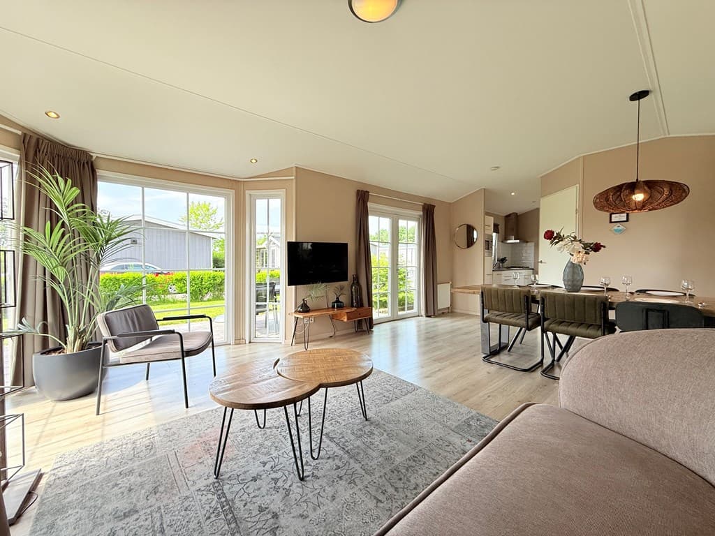 Gezellige woonkamer met grote ramen, moderne meubels en open keuken, uitzicht op groene omgeving van vakantiepark De Beemster