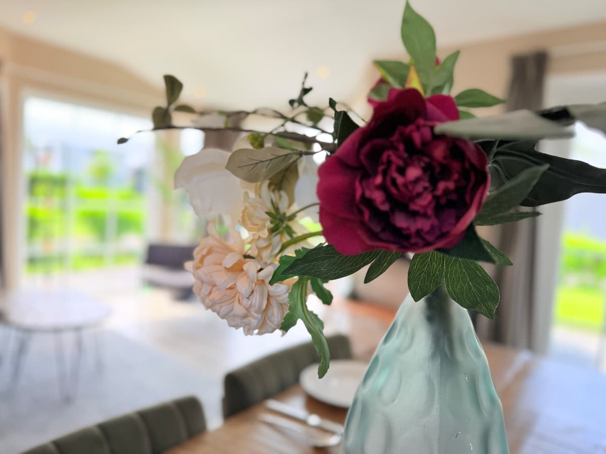 Tafel met een vaas met bloemen, op de achtergrond een lichte woonkamer met grote ramen en zicht op het tapeet.
