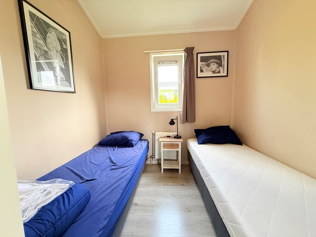 Slaapkamer met twee eenpersoonsbedden, een nachtkastje en wanddecoratie met zwart-wit foto's.