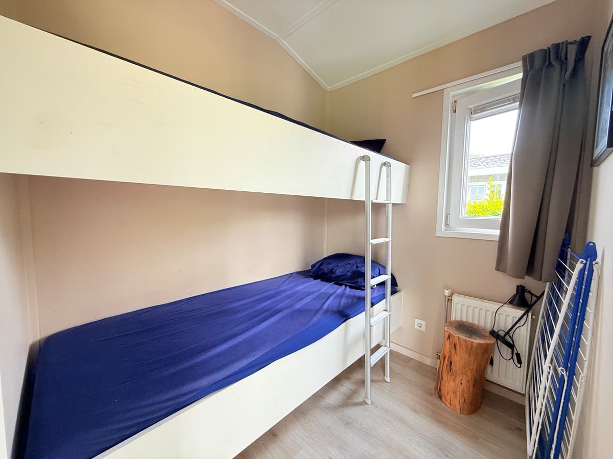 Slaapkamer met stapelbed en raam, lichte muren en houten vloer, houten blok als bijzettafel.