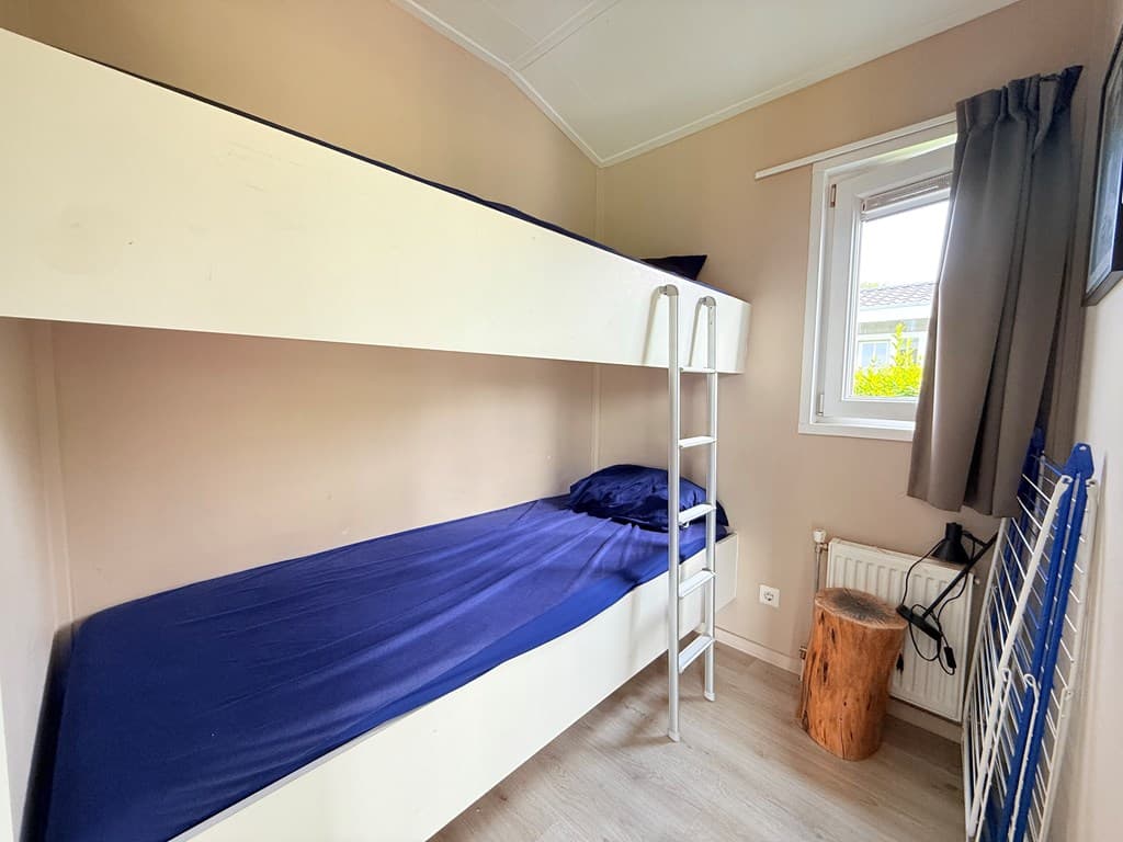 Slaapkamer met stapelbed en raam, lichte muren en houten vloer, houten blok als bijzettafel.