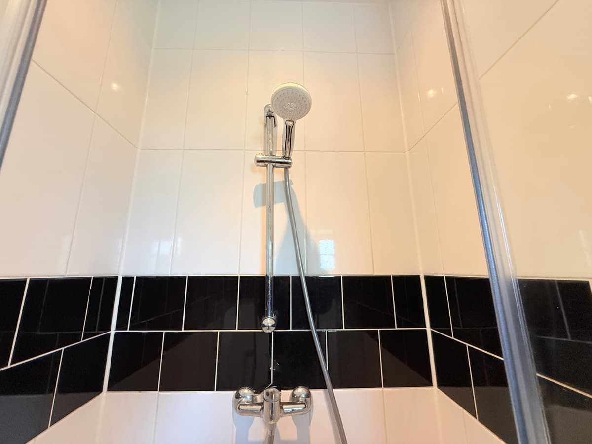 Douche met een zwarte en witte tegelwand en een handdouche in een moderne badkamer.
