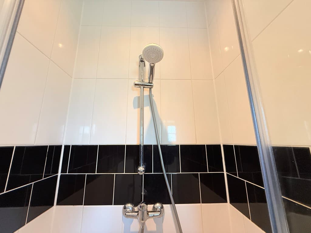 Douche met een zwarte en witte tegelwand en een handdouche in een moderne badkamer.