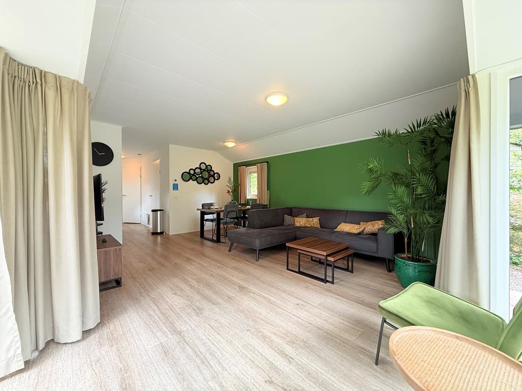 Lichte woonkamer met groene wand, comfortabele bank, eettafel en planten in EuroParcs Resort De Utrechtse Heuvelrug