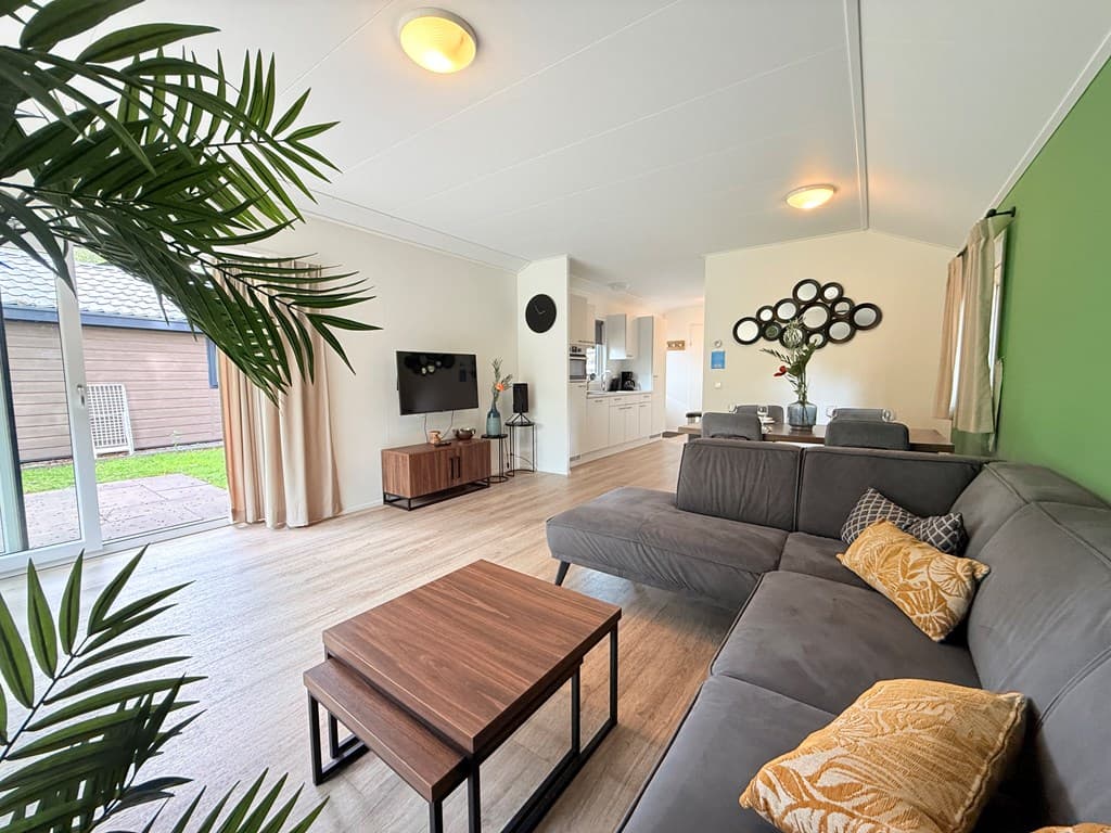 Ruime woonkamer met een comfortabele bank, tv, planten, en een zicht op de open keuken en eetruimte.