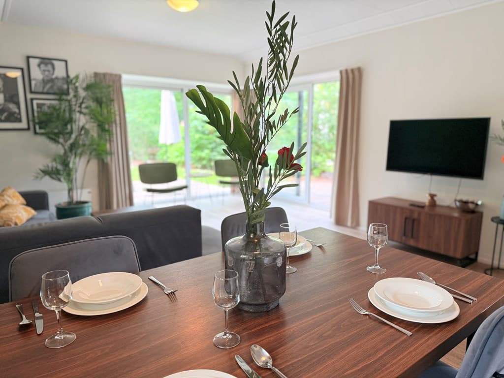 Eethoek met stijlvolle tafel, servies en een vaas met bloemen, uitzicht op groene omgeving door grote ramen.