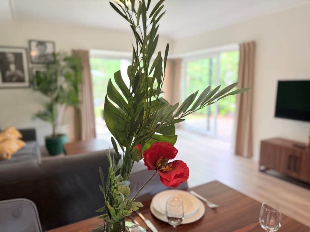 Eetkamertafel met bloemen en servies, woonkamer op de achtergrond met grote ramen en moderne inrichting