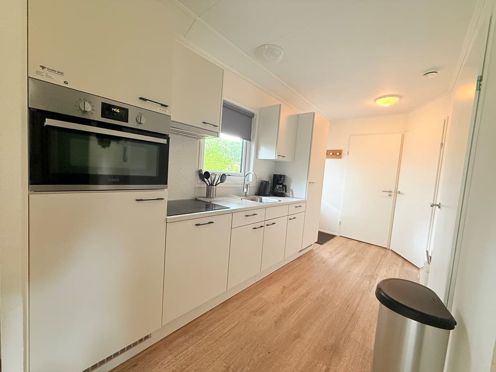 Moderne keuken met inbouwapparatuur, witte kasten en houten vloer in lichte ruimte met natuurlijk licht.