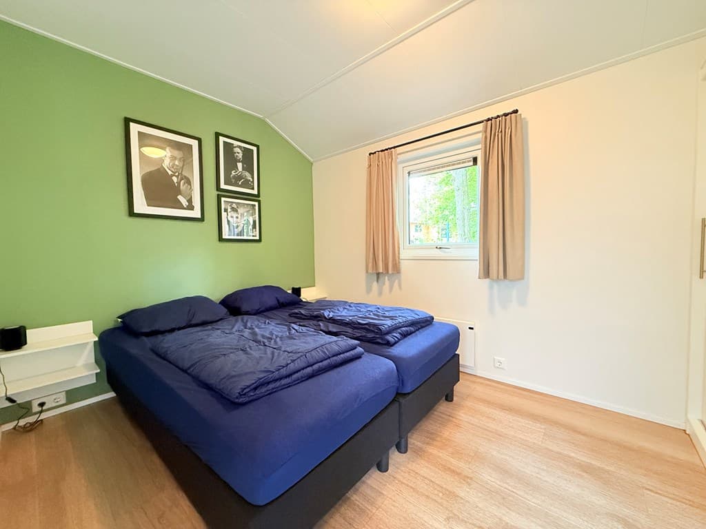 Slaapkamer met twee eenpersoonsbedden, groene wand, gordijnen en foto's aan de muur.