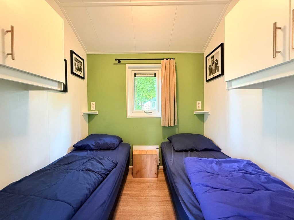 Slaapkamer met twee eenpersoonsbedden en groene muur, raam met gordijn en zwarte en witte foto's aan de muur.