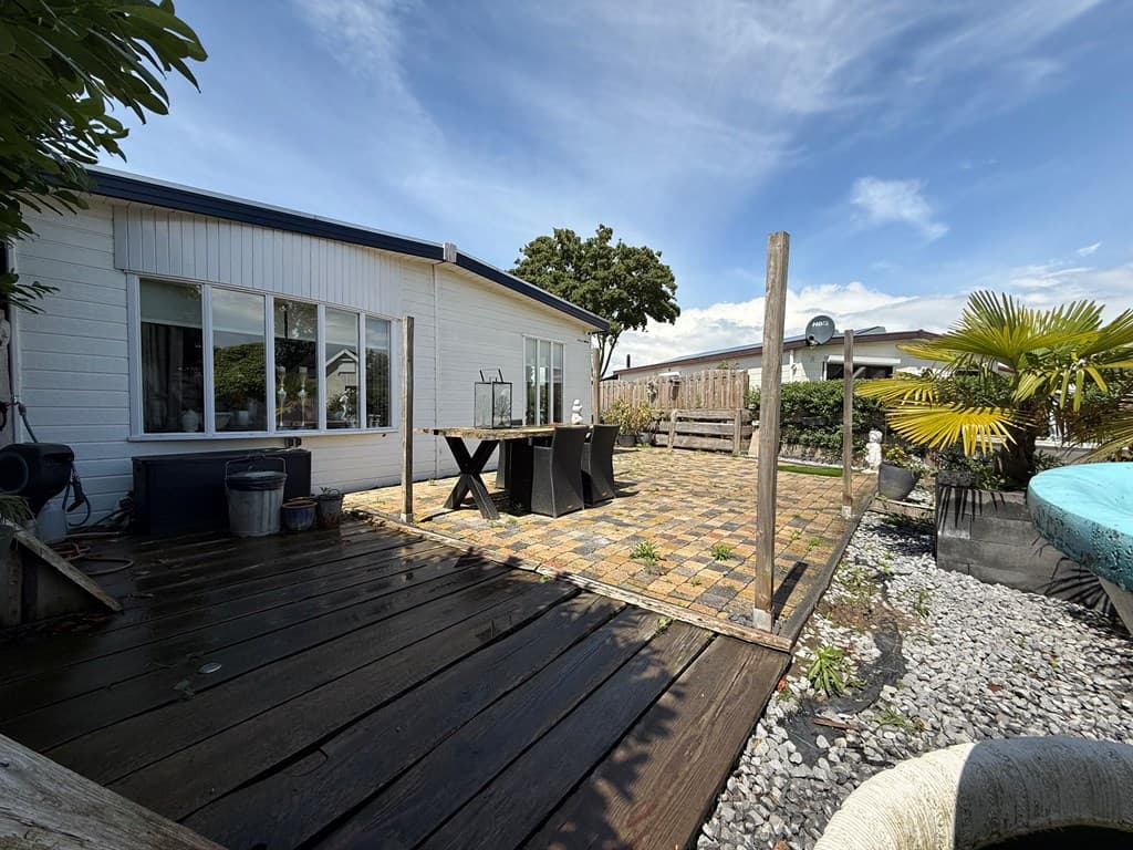 Terras met houten vlonders en stenen tegels, planten, een tafel met stoelen en een uitzicht op een andere hortus.