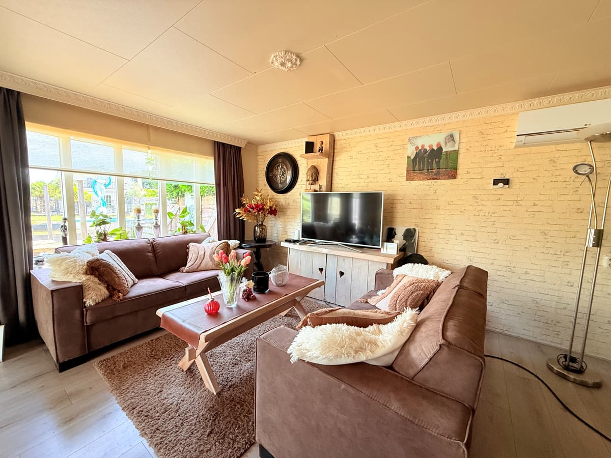 Gezellige woonkamer met twee bruine bankstellen, een tv op een kast en een houten salontafel met decoraties.