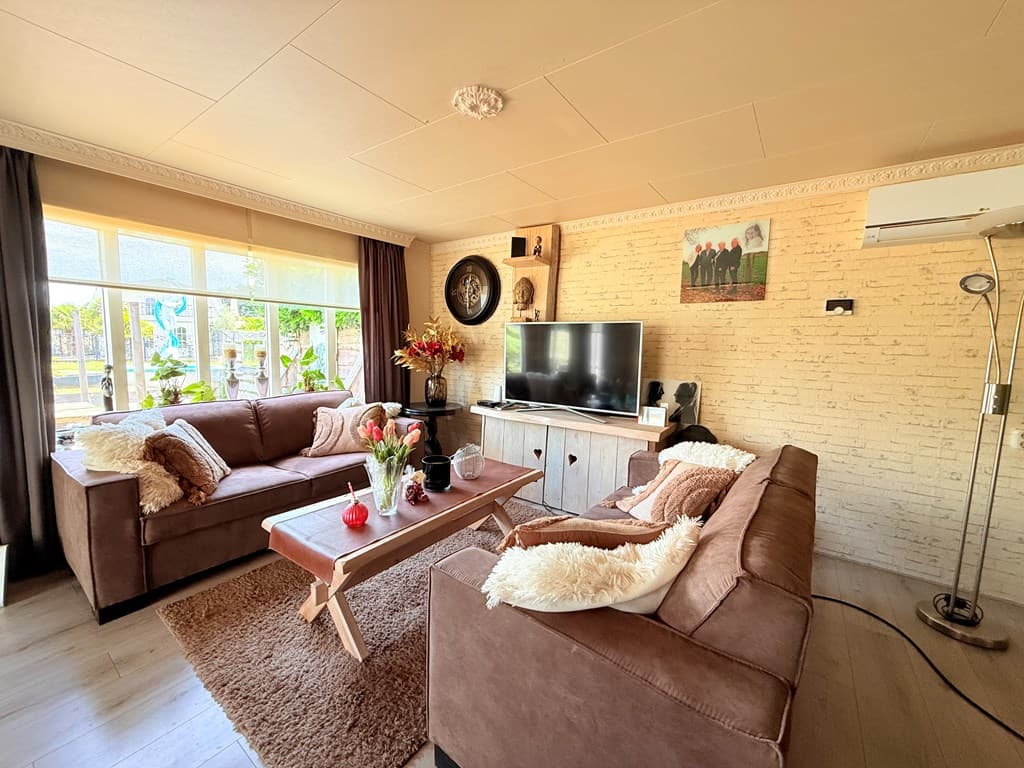 Gezellige woonkamer met twee bruine bankstellen, een tv op een kast en een houten salontafel met decoraties.