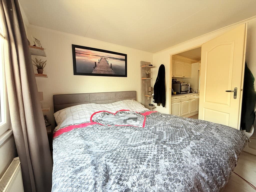 Slaapkamer met een groot bed, een schilderij aan de wand en zicht op een keukenruimte in de achtergrond
