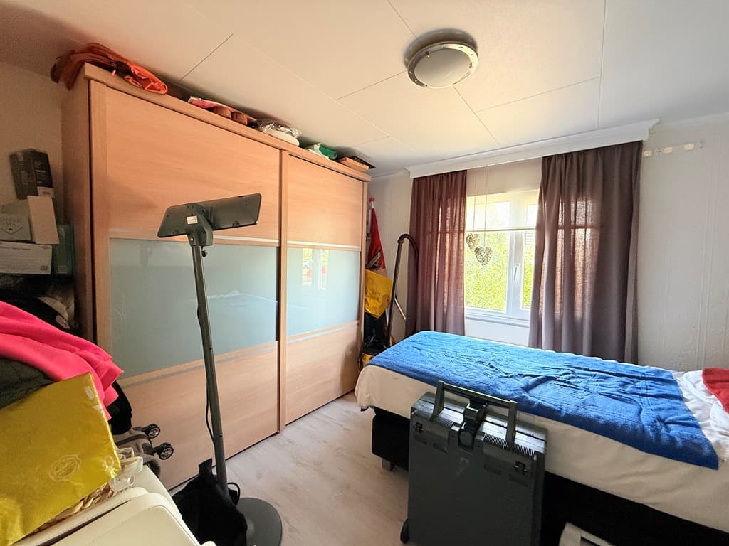 Slaapkamer met een bed, kledingkast en raam met lange gordijnen, enkele persoonlijke spullen zichtbaar