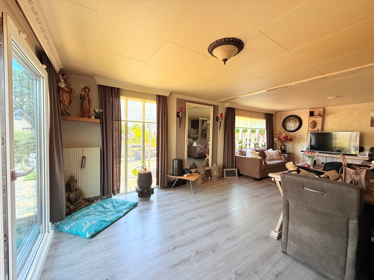 Zicht op een lichte woonkamer met grote ramen, comfortabele banken en decoratieve elementen zoals beelden en een spiegel