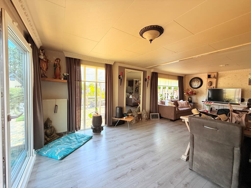 Zicht op een lichte woonkamer met grote ramen, comfortabele banken en decoratieve elementen zoals beelden en een spiegel