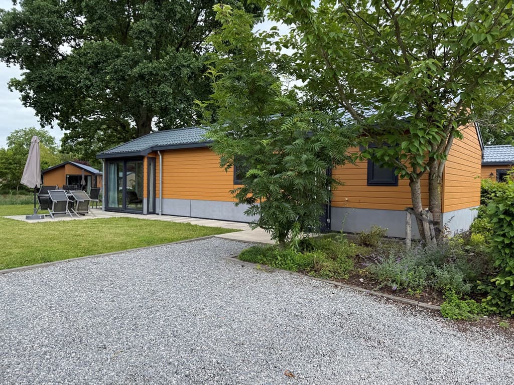 Vakantiehuis met oranje gevel, een tuin met gras, grijze grindpad en terras met tuinmeubilair onder een parasol.