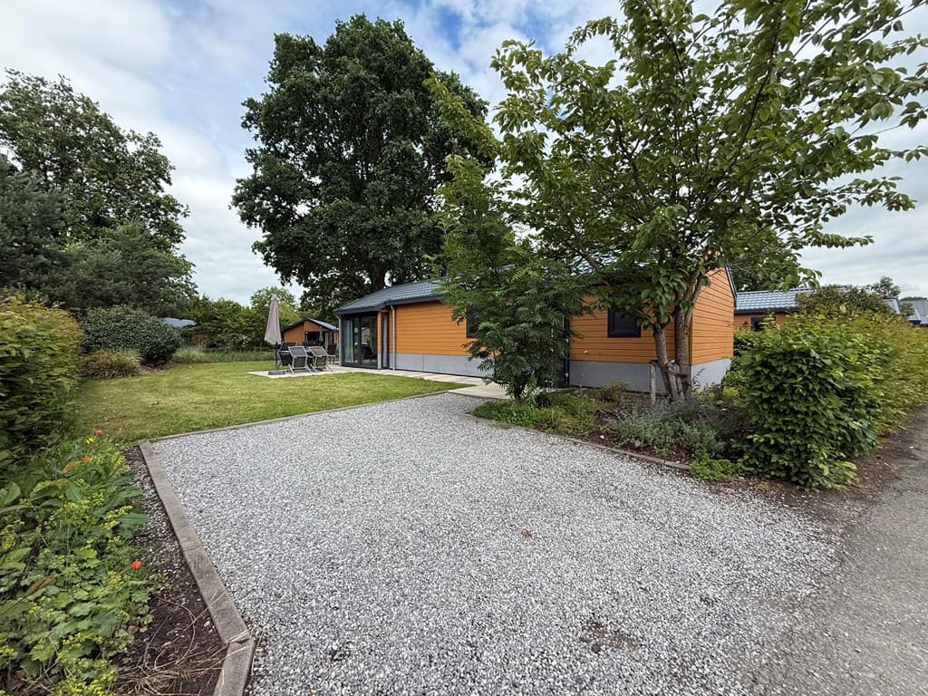 Oranje vakantiehuis met tuin en terras, omringd door groen en grindpad op EuroParcs Zuiderzee in Biddinghuizen