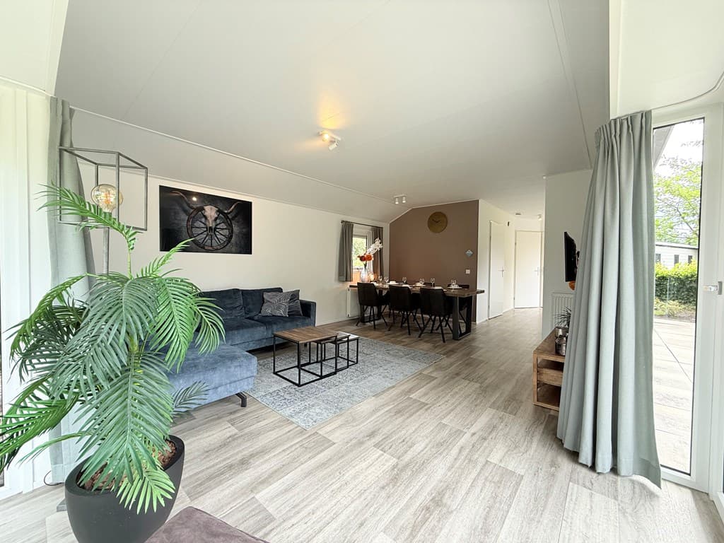 Moderne woonkamer met een bank, eettafel en een plantenpot, toegang tot buiten en grote ramen voor natuurlijk licht