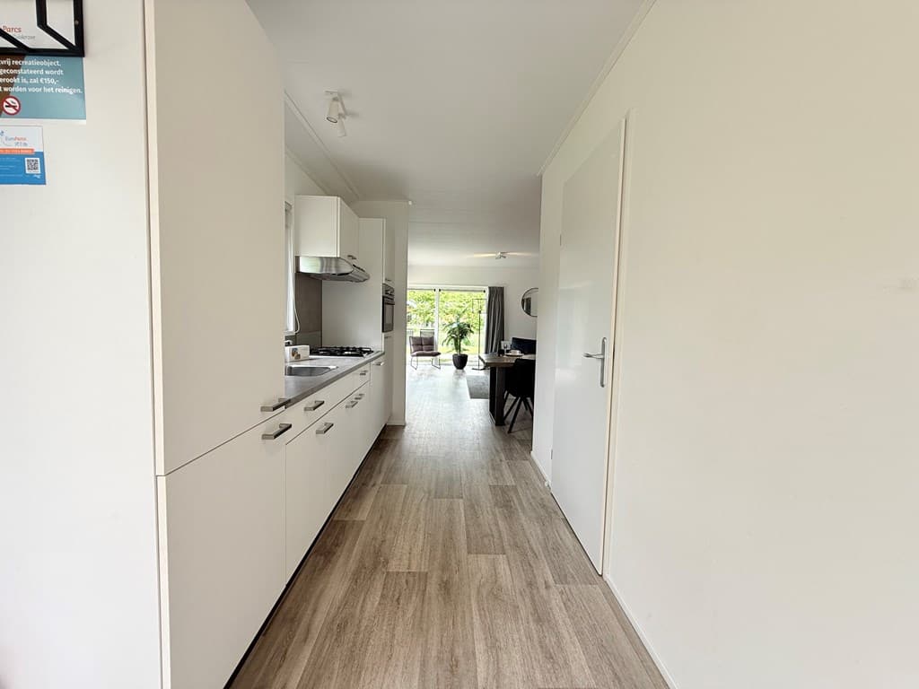 Hal met uitzicht op moderne woonkamer en keuken, lichte vloer en witte muren, natuurlijke verlichting van buitenaf