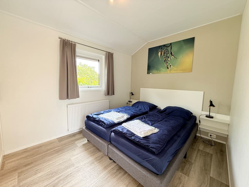 Slaapkamer met twee eenpersoonsbedden, raam met gordijnen en een schilderij aan de muur