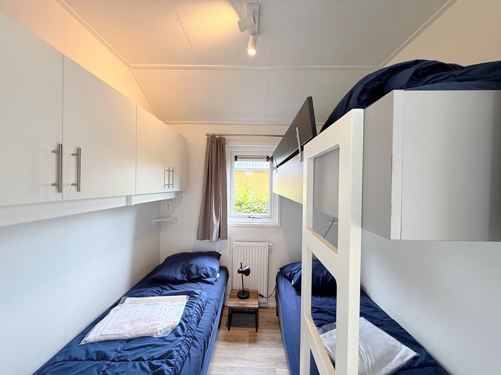 Slaapkamer met twee eenpersoonsbedden, bovenbed, wandkasten en raam met gordijnen.