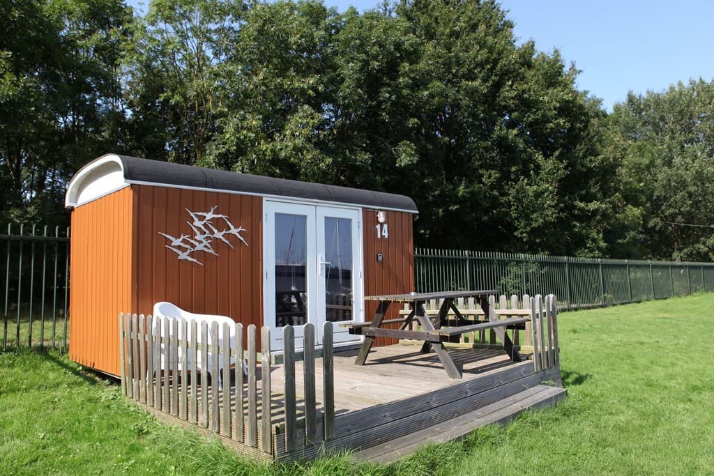 Houten vakantiehuis met een terras, picknicktafel en omheining, gelegen in een groene omgeving nabij een jachthaven