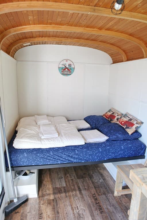 Slaapruimte met twee bedden, houten plankenvloer en houten plafond, eenvoudige inrichting met kussens en dekens.