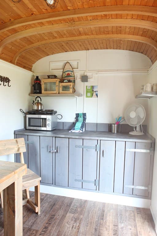Keukenruimte met houten kasten, magnetron, kookplaat en houten tafel met stoelen in een lichte, houten omgeving