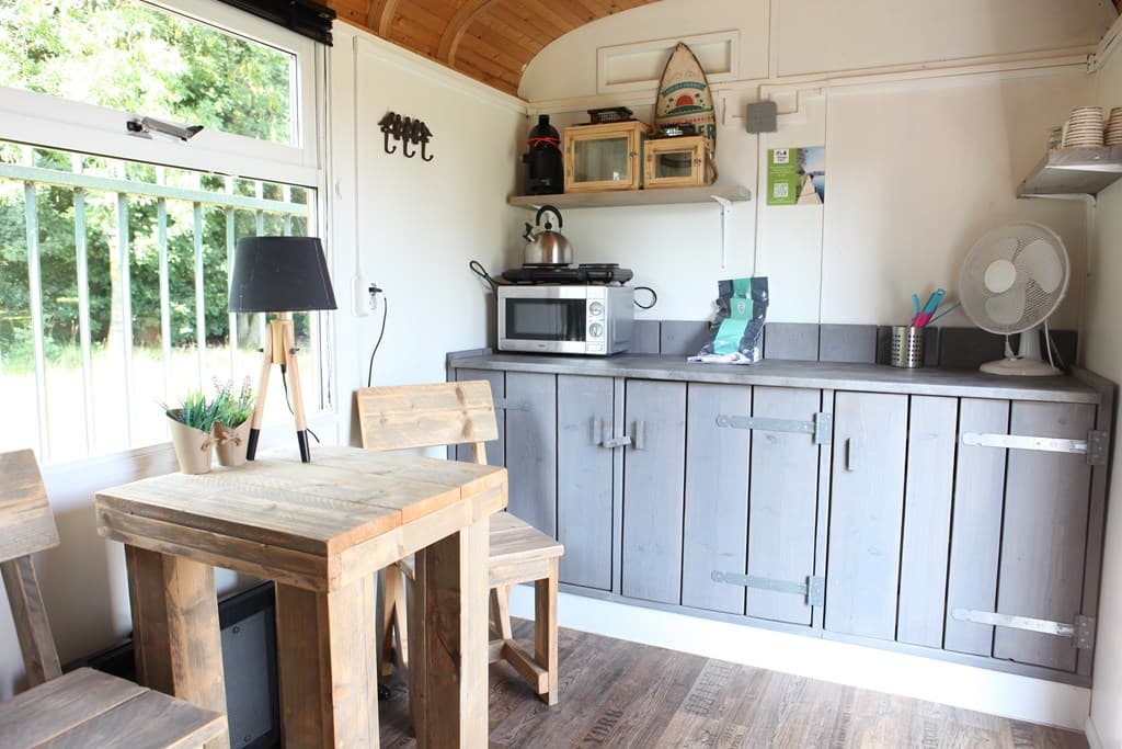 Binnenzicht van een moderne keuken met houten meubels, een eettafel, en kastjes met een microgolf en kookgerei