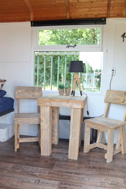 Houten tafel met twee stoelen en een lamp, uitzicht op de tuin door een groot raam