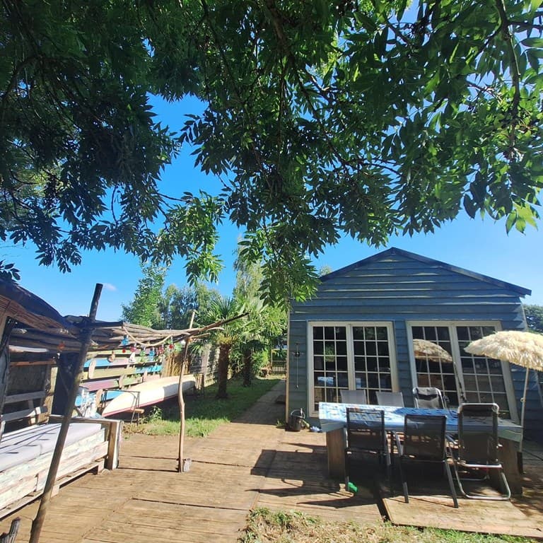 Houten vakantiehuis met een tuin, tafel en stoelen onder parasols, omringd door bomen en groene begroeiing