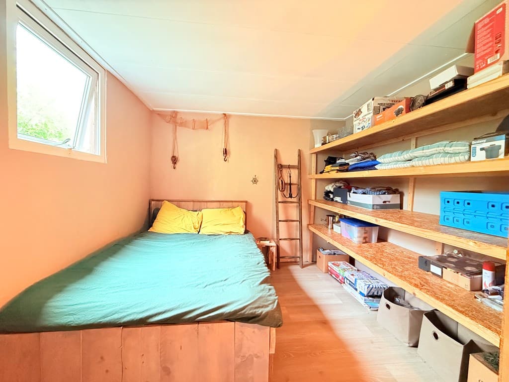 Slaapkamer met een tweepersoonsbed, houten planken met opbergruimte en een raam voor natuurlijk licht.