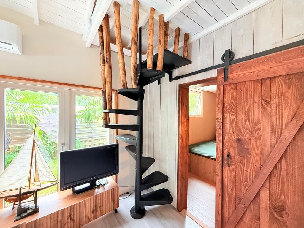 Interieur van een vakantiewoning met een wenteltrap, houten deur en uitzicht op groen aan de buitenkant.