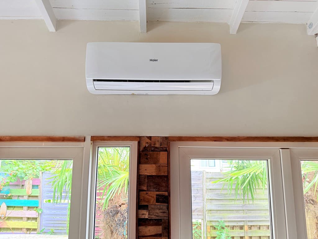Wandunit airconditioning aan de muur met uitzicht op het groen door de ramen.