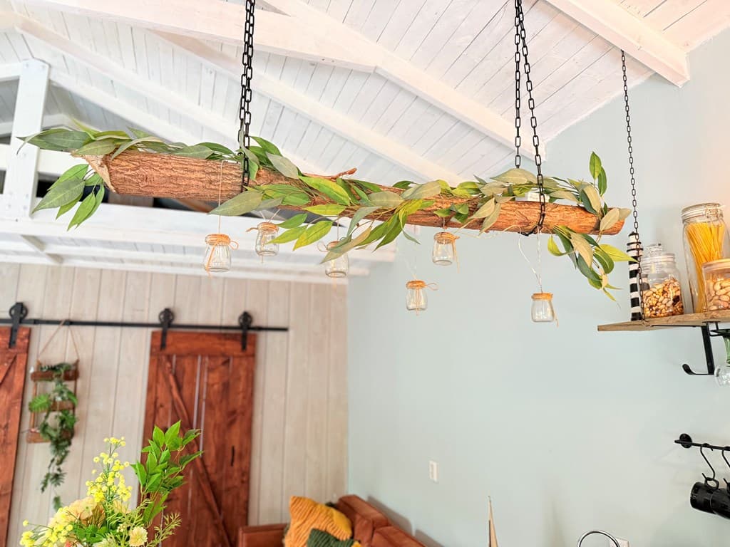 Houten balk met groene bladeren en hangende glazen potjes aan het plafond in een vakantiewoning