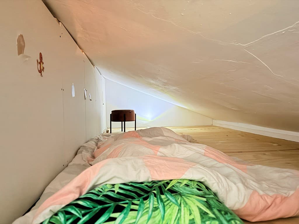 Sfeervolle slaapkamer op zolder met schuin dak, ligt een bed met dekens en een klein tafeltje in de hoek