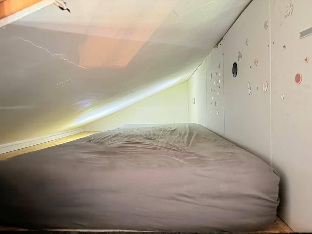 slaapruimte met een laag plafond en een bed met een grijze deken op de vloer