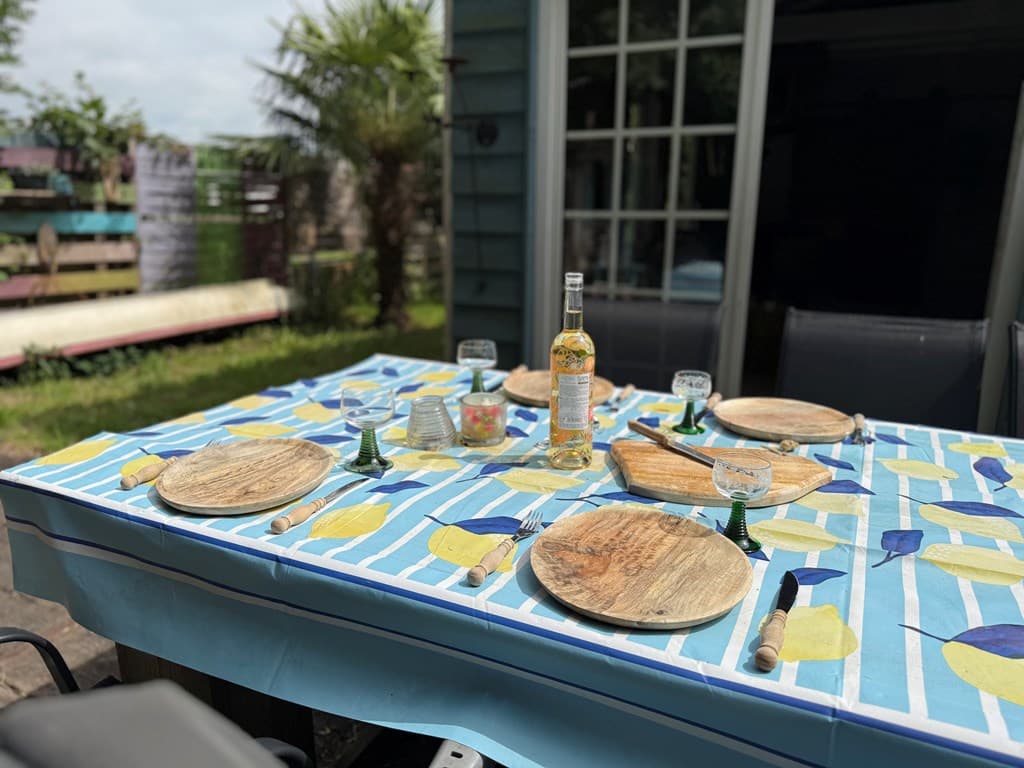 Tafel met kleurrijke tafelkleed, borden, glazen en een fles wijn in de buitenruimte van Camping ’t Wisentbos