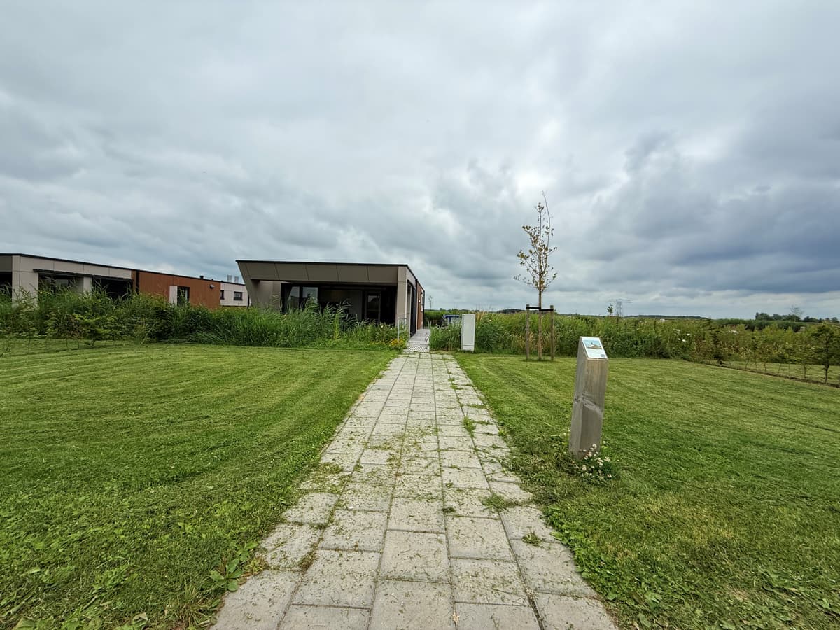 Moderne vakantiewoning met een betegeld pad, omgeven door gras en enkele bomen onder een bewolkte lucht