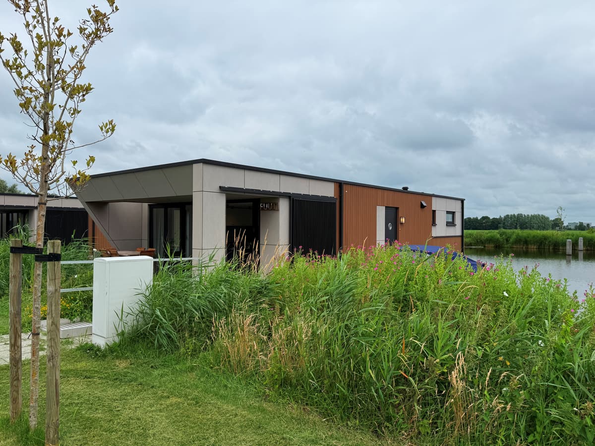 Moderne vakantiewoning met een combinatie van hout en steen, omgeven door groen en nabij water.