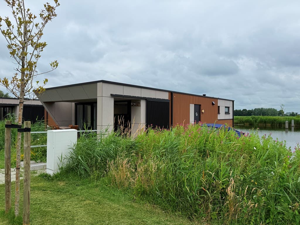Moderne vakantiewoning met een combinatie van hout en steen, omgeven door groen en nabij water.
